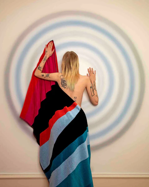Bare-backed figure holding a striped textile in front of concentric circles